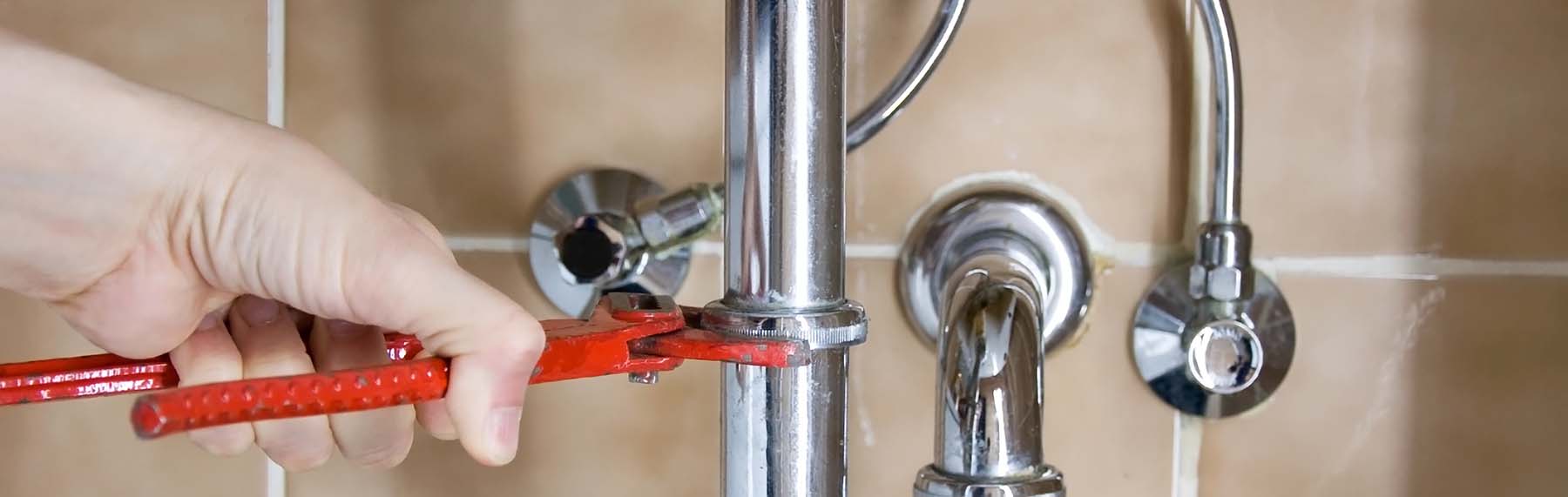 Plumber holding wrench fixing pipe under bathroom sink